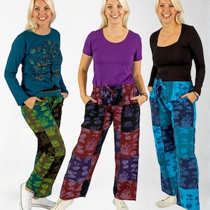 Puede incluir: Tres mujeres con pantalones patchwork coloridos y tops. Los pantalones presentan patrones de hongos y otros motivos naturales en varios colores. Las blusas incluyen una camiseta de manga larga verde azulado con un diseño de árbol, una camiseta morada y una camiseta negra de manga larga.