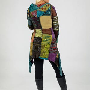 May include: A colourful patchwork hooded jacket in shades of teal, purple, brown, and yellow. The jacket has a long, flowing design and is worn with black leggings and black boots.