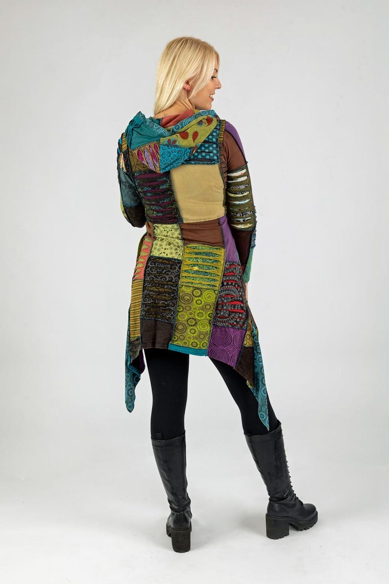 May include: A colourful patchwork hooded jacket in shades of teal, purple, brown, and yellow. The jacket has a long, flowing design and is worn with black leggings and black boots.