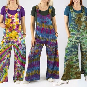Op de afbeelding: Drie tie-dye overalls in levendige kleuren. Eén paar heeft een vlinderpatroon, een ander heeft een wervelend paars en blauw ontwerp, en de derde heeft een groene en bruine paddenstoelenprint. Elke overall heeft wijde pijpen en verstelbare bandjes.