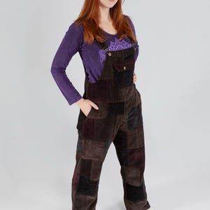 May include: A woman wearing a purple long-sleeve shirt and brown patchwork corduroy overalls. The overalls have pockets and adjustable straps. The woman is also wearing white sneakers.