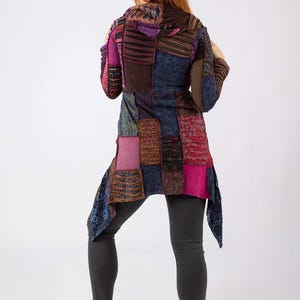 May include: A patchwork tunic in shades of purple, brown, and blue. The tunic features a variety of textured fabrics and patterns, with a long, asymmetrical hemline. The person is wearing black leggings and white trainers.
