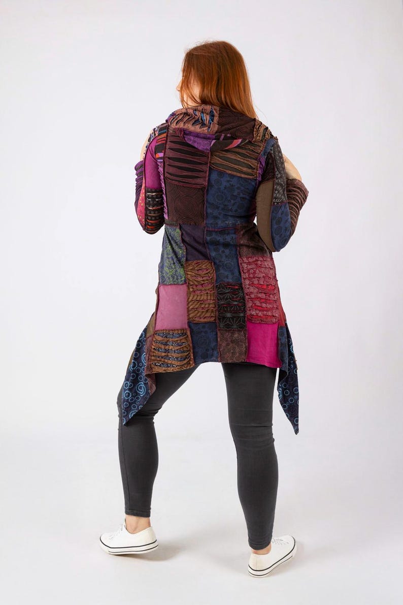 May include: A patchwork tunic in shades of purple, brown, and blue. The tunic features a variety of textured fabrics and patterns, with a long, asymmetrical hemline. The person is wearing black leggings and white trainers.
