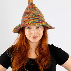 May include: A multi-coloured crochet hat with a tall, pointed crown and a wide brim. The hat displays a vibrant mix of rainbow hues, including red, orange, yellow, green, blue, and purple. A unique, handmade accessory.
