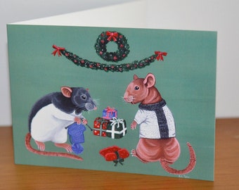 May include: A Christmas card featuring two rats dressed in sweaters. The rat on the left is black and white and is holding a blue knitted scarf. The rat on the right is brown and is wearing a white and black striped sweater. Both rats are standing in front of a green background with a Christmas wreath and garland.