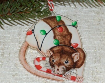 May include: A Christmas ornament featuring a brown and white rat wearing a string of colorful Christmas lights and holding a candy cane.