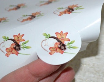 May include: A sheet of white sticker paper with a repeating pattern of round stickers featuring a white rat with orange lilies. One sticker is peeled back to show the design.