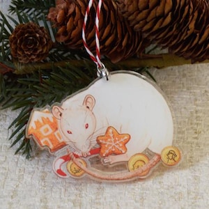 May include: White rat Christmas ornament with a red nose, holding a gingerbread star and candy cane. The ornament is made of clear acrylic and has a red and white string for hanging.