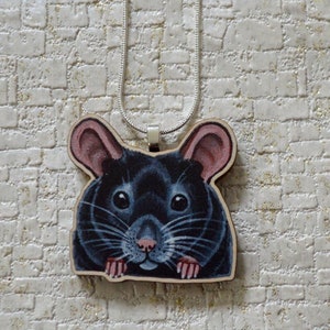 May include: A black rat face pendant necklace with a silver chain. The rat is looking directly at the camera with a curious expression. The pendant is made of wood and has a painted finish.
