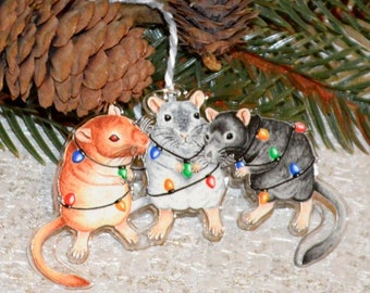 May include: Three small, wooden, Christmas ornaments shaped like mice. Each mouse is decorated with colorful Christmas lights. The mice are standing on a light brown, textured surface.