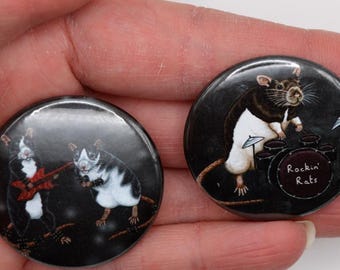 May include: Two round black and white buttons with images of rats playing musical instruments. The first button shows two rats, one playing a guitar and the other playing a keyboard. The second button shows a rat playing a drum set with the text "Rockin' Rats".