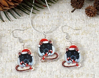 May include: A silver necklace and earrings set featuring a Christmas rat design. The rat is wearing a Santa hat and holding a candy cane. The jewelry is displayed with pine cones and evergreen branches.