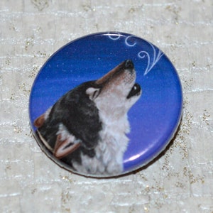 May include: A round button with a blue background and a white wolf howling at the moon. The wolf is black and white and has a white collar.