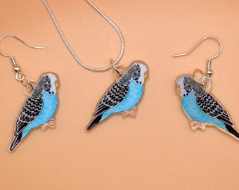 Può includere: Un set di collana e orecchini in argento con ciondoli di parrocchetti blu e grigi. I parrocchetti hanno occhi neri e becchi gialli.