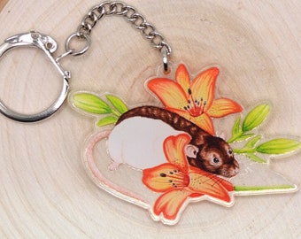 May include: A white and brown rat with orange lily flowers, a green stem, and leaves on a clear acrylic keychain with a silver metal ring.