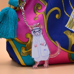 May include: A white lab coat with a teal tassel keychain featuring a cartoon rat wearing a lab coat and goggles.