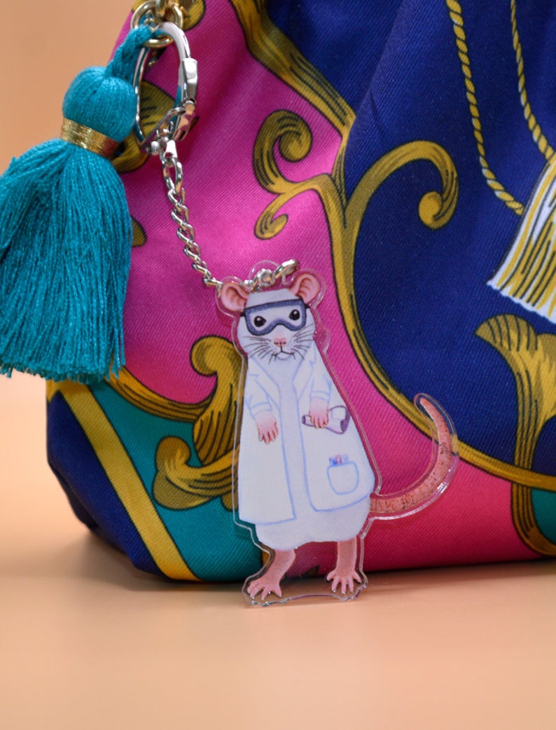May include: A white lab coat with a teal tassel keychain featuring a cartoon rat wearing a lab coat and goggles.