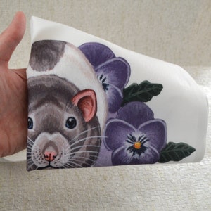 May include: White fabric with a watercolour illustration of a rat. The rat has a grey and white coat, pink ears, and blue eyes. The design includes purple pansies and green leaves, creating a floral and animal-themed pattern.