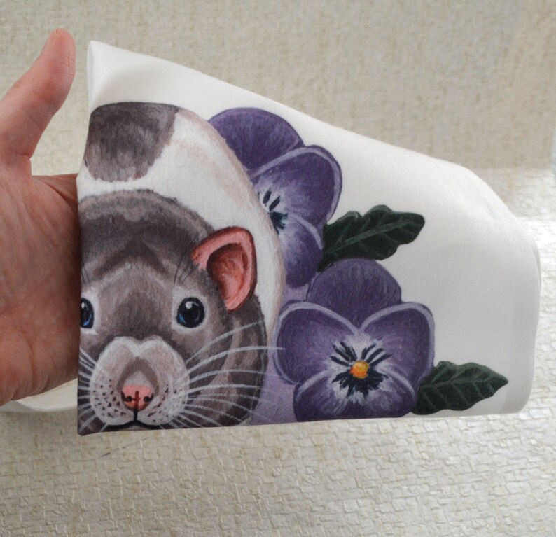 May include: White fabric with a watercolour illustration of a rat. The rat has a grey and white coat, pink ears, and blue eyes. The design includes purple pansies and green leaves, creating a floral and animal-themed pattern.
