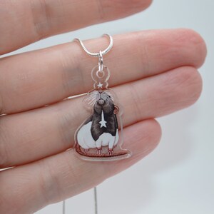 May include: A silver chain necklace with a clear acrylic pendant featuring a hand-painted illustration of a black and white rat with a star on its chest.