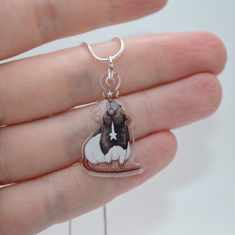 May include: A silver chain necklace with a clear acrylic pendant featuring a hand-painted illustration of a black and white rat with a star on its chest.