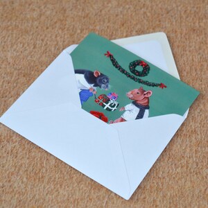 May include: A Christmas card featuring two mice wearing winter clothes and exchanging gifts. The card has a green background with a garland and a wreath.