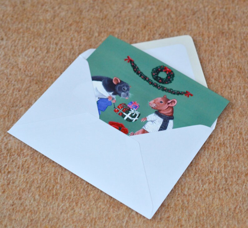 May include: A Christmas card featuring two mice wearing winter clothes and exchanging gifts. The card has a green background with a garland and a wreath.