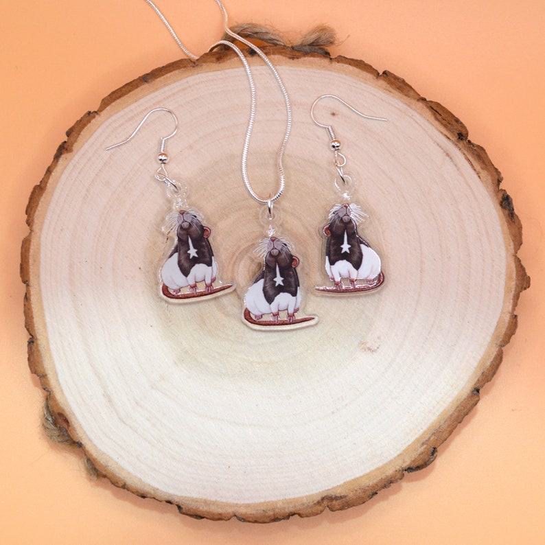 May include: A silver necklace and earrings set featuring a black and white rat design. The rat is depicted with a star on its chest and is set against a clear background.