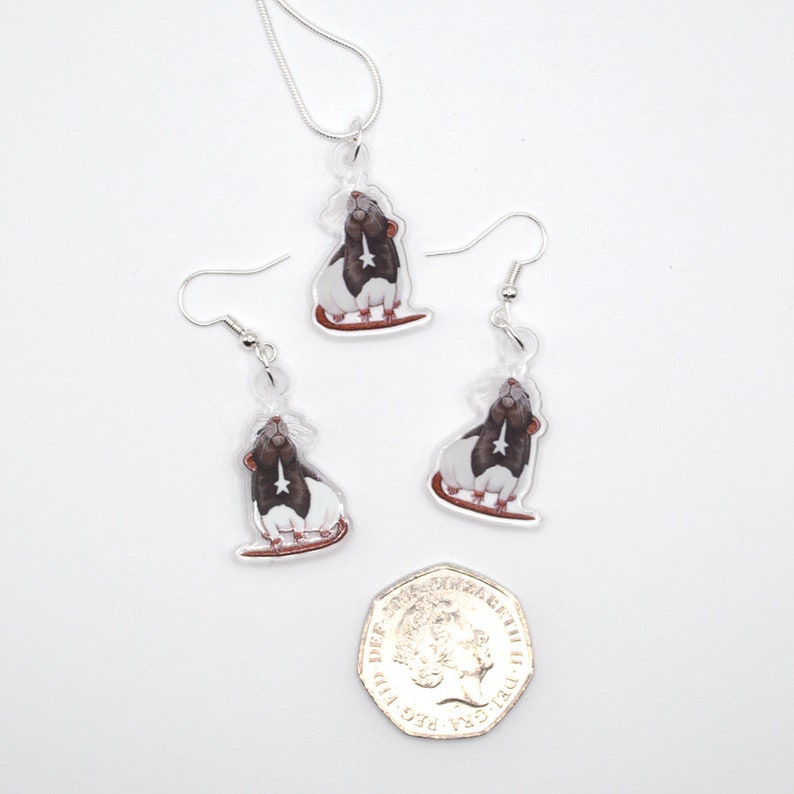 May include: A set of silver rat earrings and a necklace. The rat charms are black and white with a silver star on their chest. The earrings and necklace are hanging from a white background.