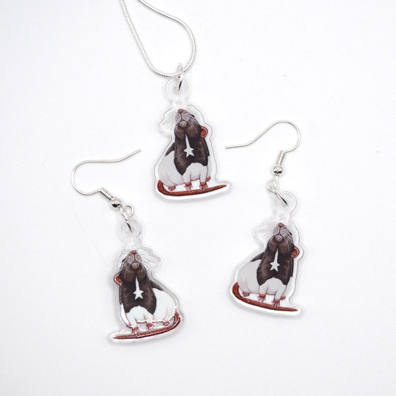 May include: A set of silver rat earrings and a necklace. Each piece features a black and white rat with a star on its chest, looking up.