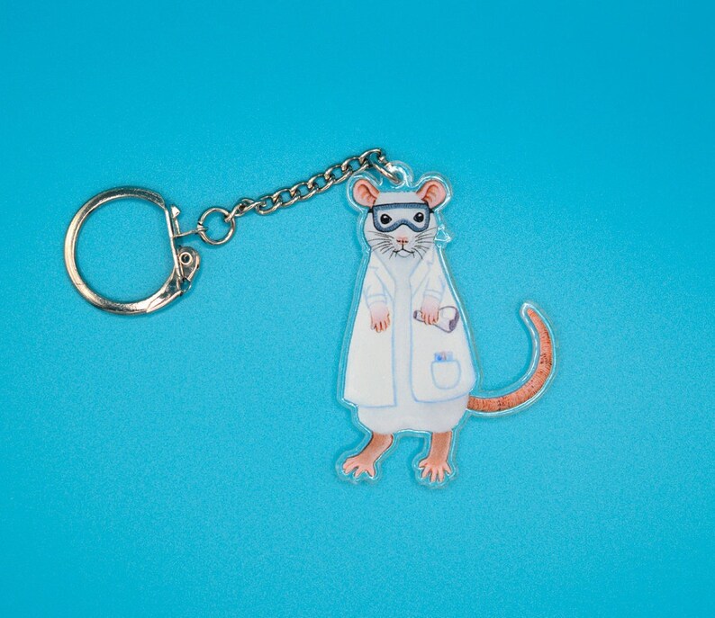 May include: A white lab coat keychain featuring a cartoon mouse wearing goggles and holding a test tube. The mouse has a brown tail and pink ears.