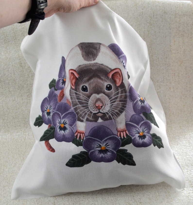 May include: White fabric bag with a detailed illustration of a rat and purple pansies. The rat has a brown and white coat, pink ears and nose. The pansies have yellow centres and green leaves.