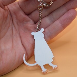 May include: A white acrylic keychain shaped like a sitting mouse. The keychain is attached to a silver chain and a silver key ring.