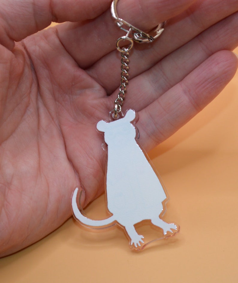 May include: A white acrylic keychain shaped like a sitting mouse. The keychain is attached to a silver chain and a silver key ring.