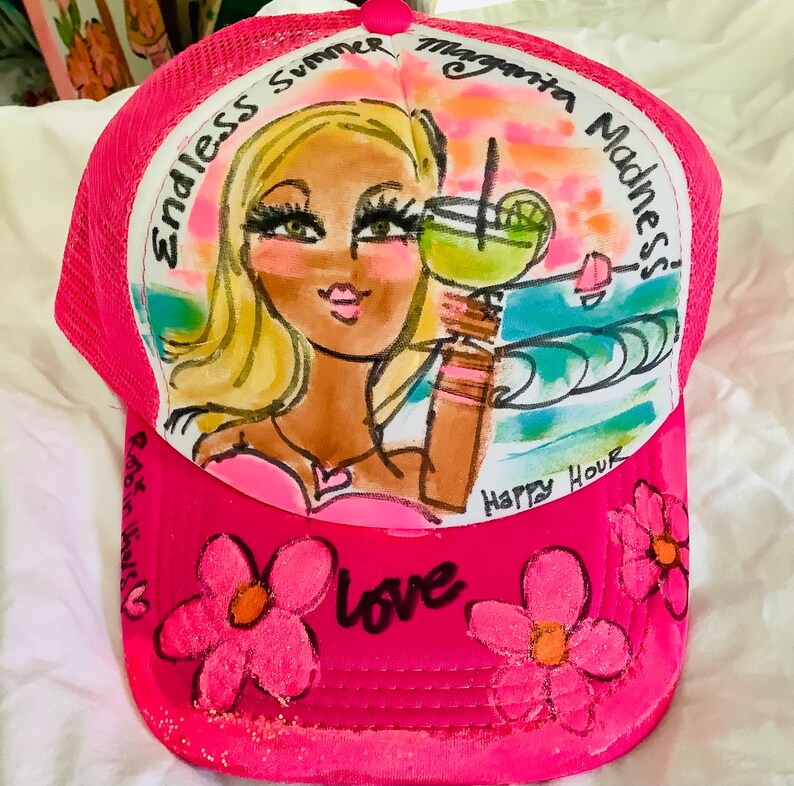 K&ouml;nnte beinhalten: Rosa-farbener Netz-Trucker-Hut mit handgemaltem Design einer Frau mit blonden Haaren, die ein Margarita-Glas h&auml;lt. Der Hut tr&auml;gt den Text "Endless Summer Margarita Madness!" und "Happy Hour". Auf dem Hut befinden sich rosa Blumen mit dem Wort "love" in Schwarz.