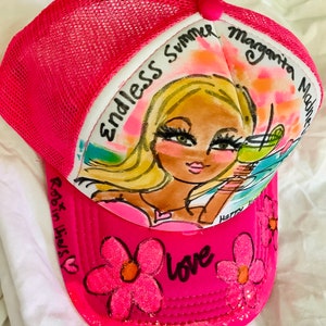 K&ouml;nnte beinhalten: Rosafarbener Trucker-Hut mit Netzr&uuml;cken. Die Vorderseite des Hutes zeigt eine handgemalte Illustration einer Frau mit blonden Haaren und einer Margarita. Der Text "Endless Summer Margarita Madness" ist auf dem Hut geschrieben. Die Worte "Robin Hicks" und "Love" sind ebenfalls auf dem Hut geschrieben.