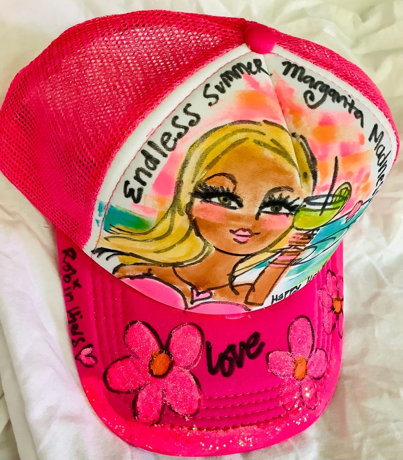 K&ouml;nnte beinhalten: Rosafarbener Trucker-Hut mit Netzr&uuml;cken. Die Vorderseite des Hutes zeigt eine handgemalte Illustration einer Frau mit blonden Haaren und einer Margarita. Der Text "Endless Summer Margarita Madness" ist auf dem Hut geschrieben. Die Worte "Robin Hicks" und "Love" sind ebenfalls auf dem Hut geschrieben.