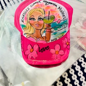 K&ouml;nnte beinhalten: Rosafarbener Trucker-Hut mit handgemaltem Design, das eine Frau mit blonden Haaren zeigt, die eine Margarita h&auml;lt, mit dem Text "Endless Summer Margarita Madness! Happy Hour Love" auf der Vorderseite.