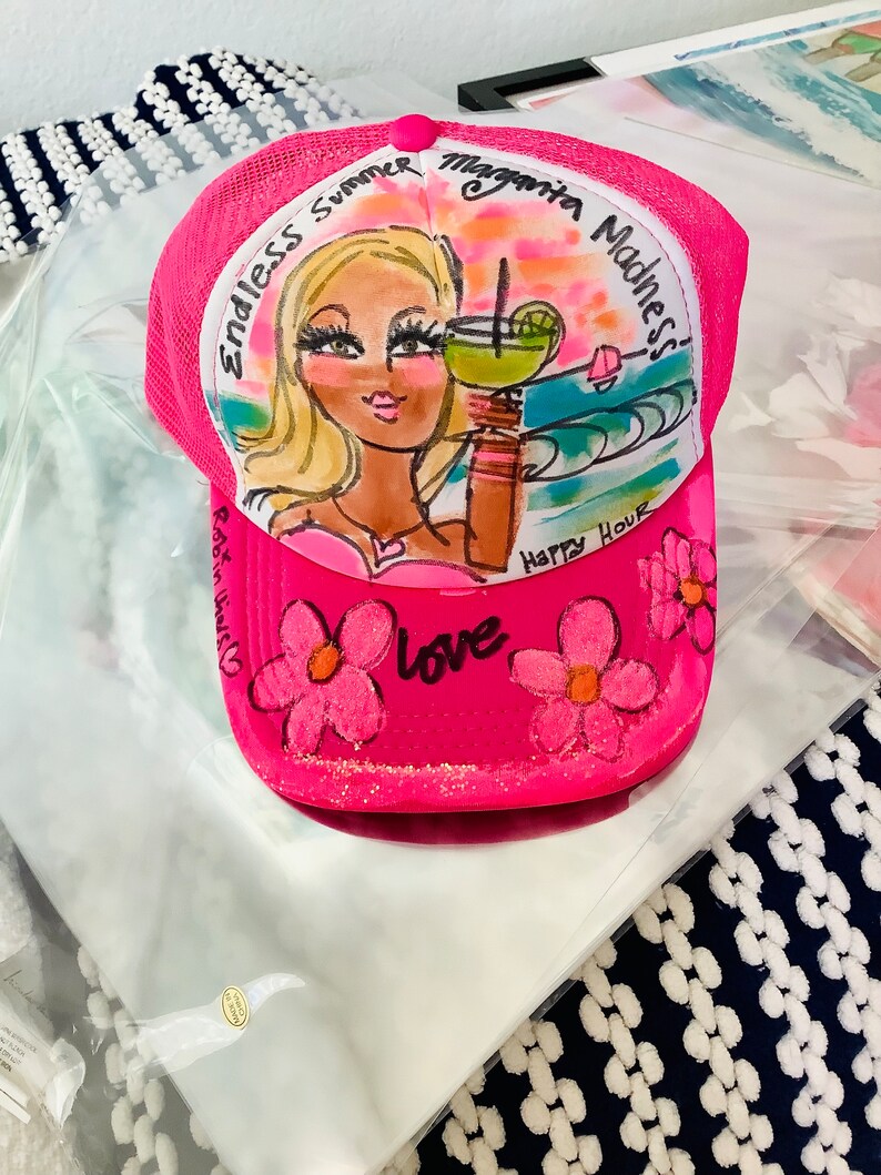 K&ouml;nnte beinhalten: Rosafarbener Trucker-Hut mit handgemaltem Design, das eine Frau mit blonden Haaren zeigt, die eine Margarita h&auml;lt, mit dem Text "Endless Summer Margarita Madness! Happy Hour Love" auf der Vorderseite.