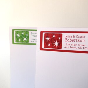 May include: Two red and green Christmas address labels with a starburst design. The text on the red label reads "Jenna & Connor Robertson 1234 Main Street Any Town, US 12345".