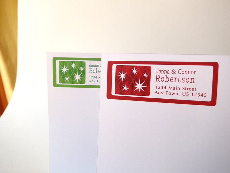 May include: Two red and green Christmas address labels with a starburst design. The text on the red label reads "Jenna & Connor Robertson 1234 Main Street Any Town, US 12345".