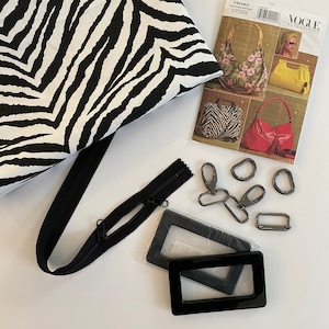 May include: A collection of sewing supplies for bag making. Includes a black and white zebra print fabric, a black zipper, metal hardware, and a Vogue pattern for various bag styles. The pattern features images of finished bags.