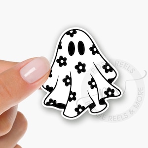 May include: An interchangeable acrylic badge reel topper in the shape of a ghost, decorated with black flower patterns. The text on the image reads "Interchangeable Acrylic Badge Reel Topper" and "Attaches with Hoop & Loop".