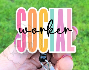 Op de afbeelding: Een kleurrijke "SOCIAL WORKER" badgehouder met een zwarte intrekbare badgehaspel. De badgehouder is gemaakt van helder plastic en heeft een regenboogkleurenschema.