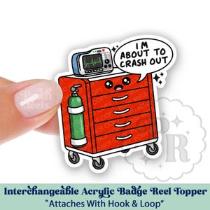 May include: A red medical cart badge reel topper with a green oxygen tank, a monitor, and the text "I'm about to crash out." The topper is an interchangeable acrylic badge reel.