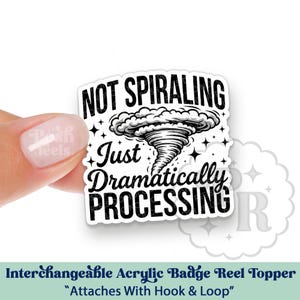 May include: A white and black acrylic badge reel topper with the text "NOT SPIRALING Just Dramatically PROCESSING" and a graphic of a tornado. The badge reel topper is held by a hand. The text "Interchangeable Acrylic Badge Reel Topper" is at the bottom.