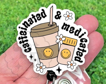 May include: A white and black round badge with a cartoon coffee cup and pill with smiley faces. The text on the badge reads "caffeinated & medicated".