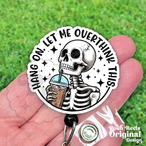 May include: A white and black badge reel with a skeleton drinking an iced coffee. The text on the badge reel says "Hang on. Let me overthink this." The badge reel has a black retractable cord and a clear plastic clip.
