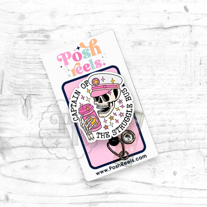 May include: A pink and white badge reel with a skeleton wearing a pink captain's hat and holding a coffee cup. The badge reel has the text "Captain of the Struggle Bus".