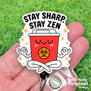 May include: A red badge reel with the text "STAY SHARP, STAY ZEN." The badge reel features a cartoon red trash can in a yoga pose with a biohazard symbol. The design includes yellow star accents and a clear plastic reel.